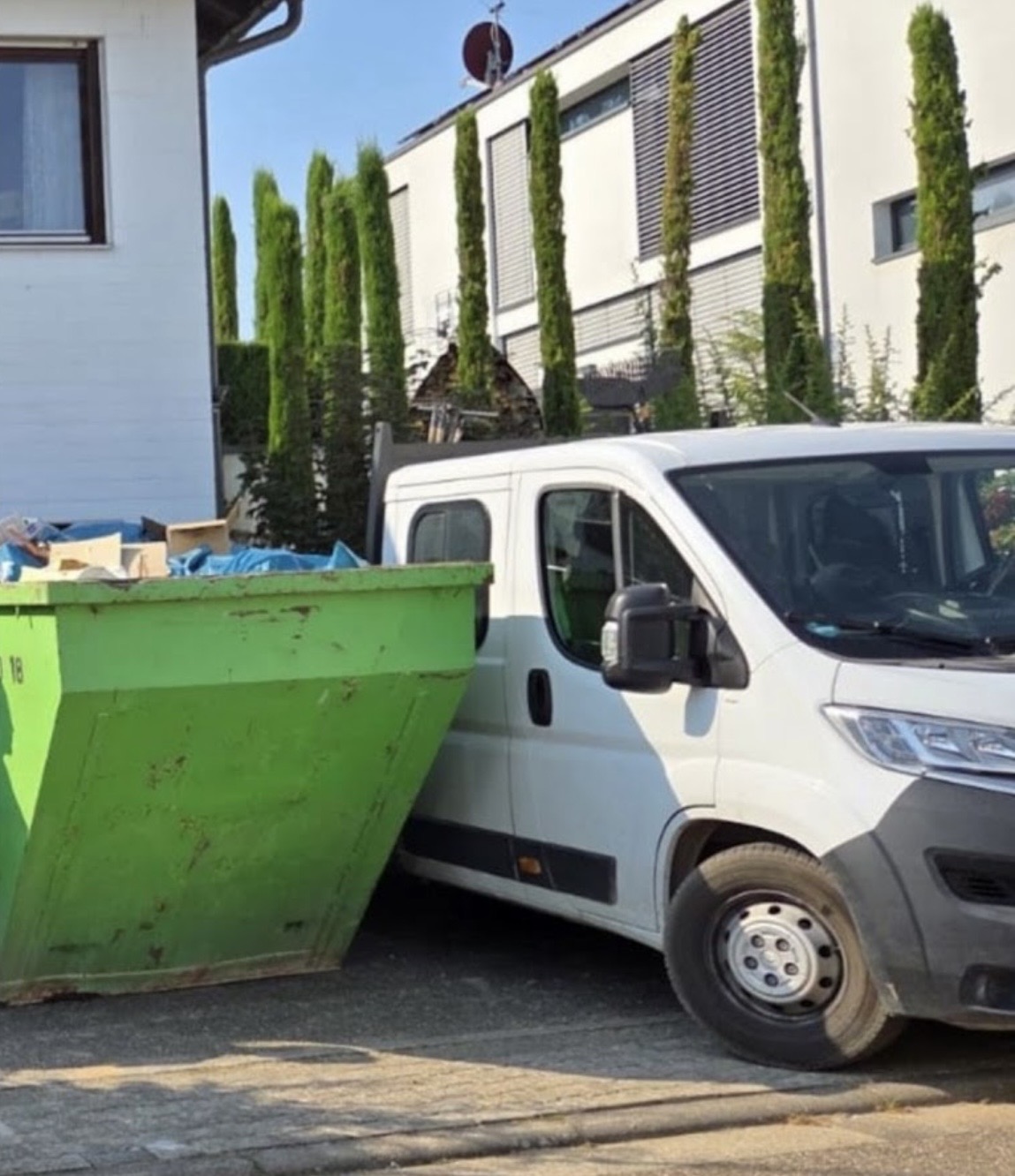 Grüner Abfallcontainer und Transporter während einer Entrümpelung